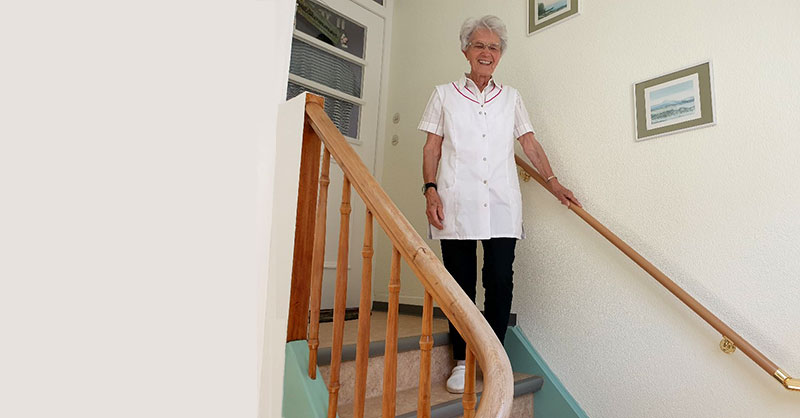 Warum beidseitiger Handlauf an Treppen Frau steht auf der letzten Stufe einer Treppe und hält sich am Handlauf fest