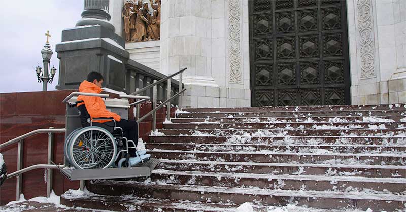 Treppenplattformlift hebt Rollstuhl über die Freitreppe einer winterlichen Kirche