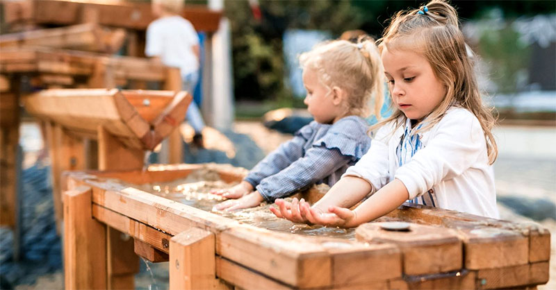 Auf einem Matschtisch planschen 2 Mädchen mit Wasser