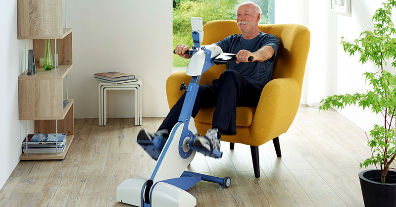 Mann im Sessel tritt in die Pedalen des Heimtrainers